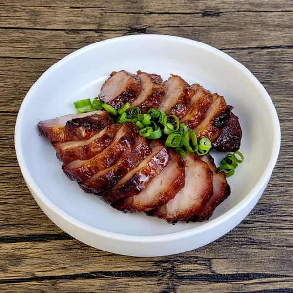 Sliced char siu (BBQ pork) with a glossy brown glaze and green onions on a white plate.