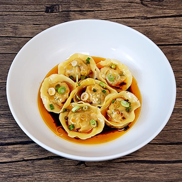 Six Brooklyn Dim Sum Co. dumplings in a white bowl, drizzled with sauce and garnished with scallions.