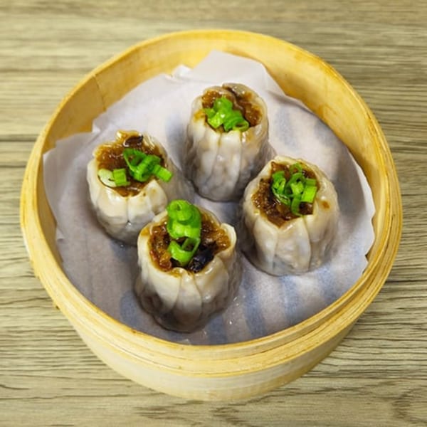 Four Brooklyn Dim Sum Co. dumplings with green onions in a bamboo steamer basket.
